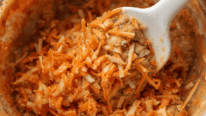 Close-up of shredded carrots and pineapple being folded into cake batter with a rubber spatula.