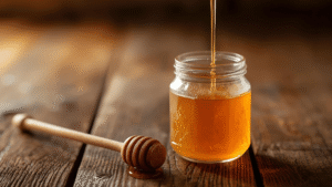 Honey sauce being poured into a glass jar with a honey dipper beside it.