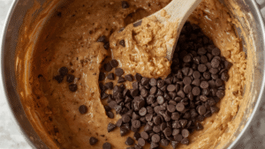 Chocolate chips folded into banana bread batter in a mixing bowl, close-up food photography, soft warm lighting.
