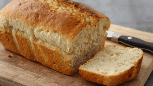 Freshly baked 4-ingredient bread loaf on a wooden cutting board, golden crust, soft inside, cozy kitchen, natural light.