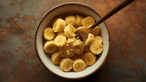 Ripe bananas being mashed with a fork in a ceramic bowl, warm kitchen lighting, rustic background.